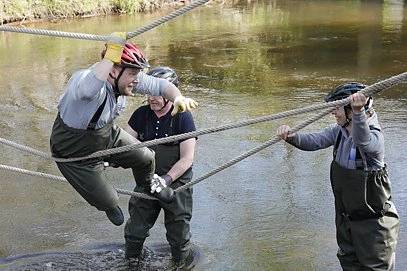 Outdoor training: employees building a rope bridge over a stream